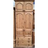 A pine wardrobe, the top section with a pair of panelled cupboard doors above a further pair of