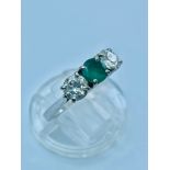 A platinum emerald and diamond three stone ring, set with a central round emerald flanked by 2 x