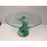 A contemporary glass dining table, with circular top, raised on a stepped, spiral support, to