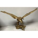 A very large brass eagle with wings outstretched perched on a log, 66 x 105cm high