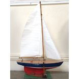A small pond yacht with hull painted red, white and blue, and white sails, raised on wooden stand,