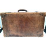 A large vintage tan leather suitcase with leather and metal studded corner protectors and travel
