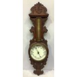 A circular brass cased aneroid barometer and thermometer mounted in foliate carved hardwood frame,