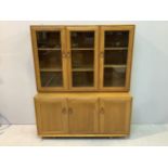 An Ercol light elm triple bookcase, the top section with glazed cupboard doors enclosing shelves,