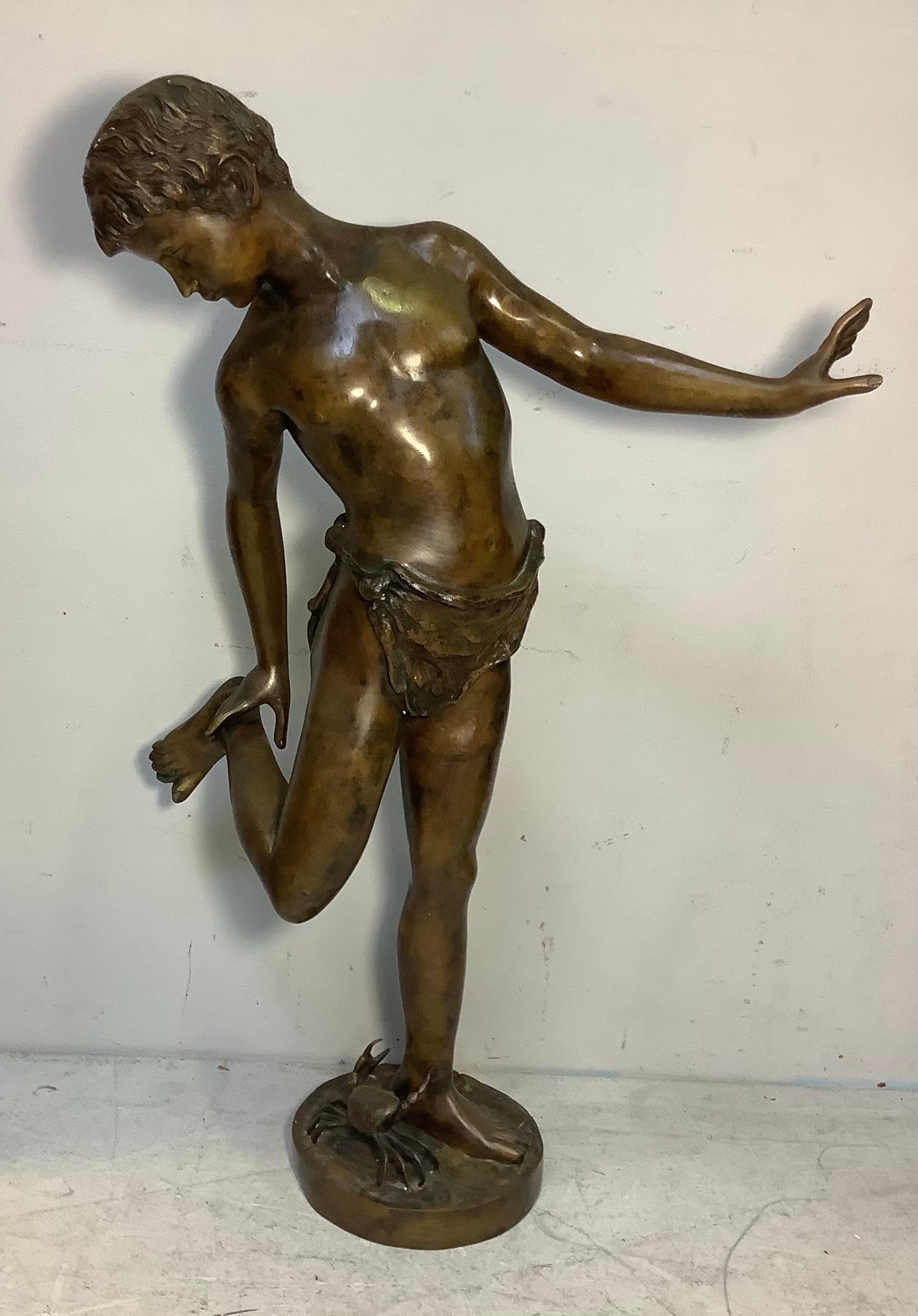 A large hollow cast bronze figure of a classical young male in loin cloth inspecting his foot