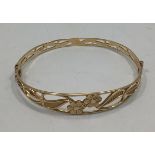 A 9ct gold hinged bangle, cast with pierced design of stylised leaves and flowers, slide catch