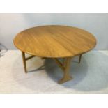 An Ercol light elm narrow drop leaf dining table with beech trestle supports, 128cm wide, together
