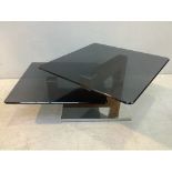 A two-tier black glass coffee table with rotating top-tier, raised on wooden support to square,