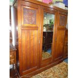 An Edwardian Walnut triple Wardrobe having a central mirror flanked by doors with carved panels