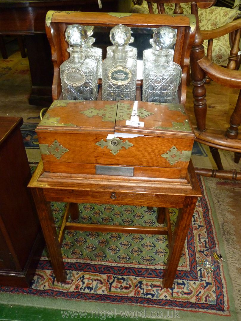 A good Oak three decanter Tantalus on a stand, mirror backed with brass fittings and carry handles.