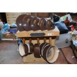 A set of five Le Creuset brown saucepans and lids in a wooden stand.