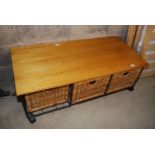 A metal framed wooden topped coffee table with three wicker baskets below.