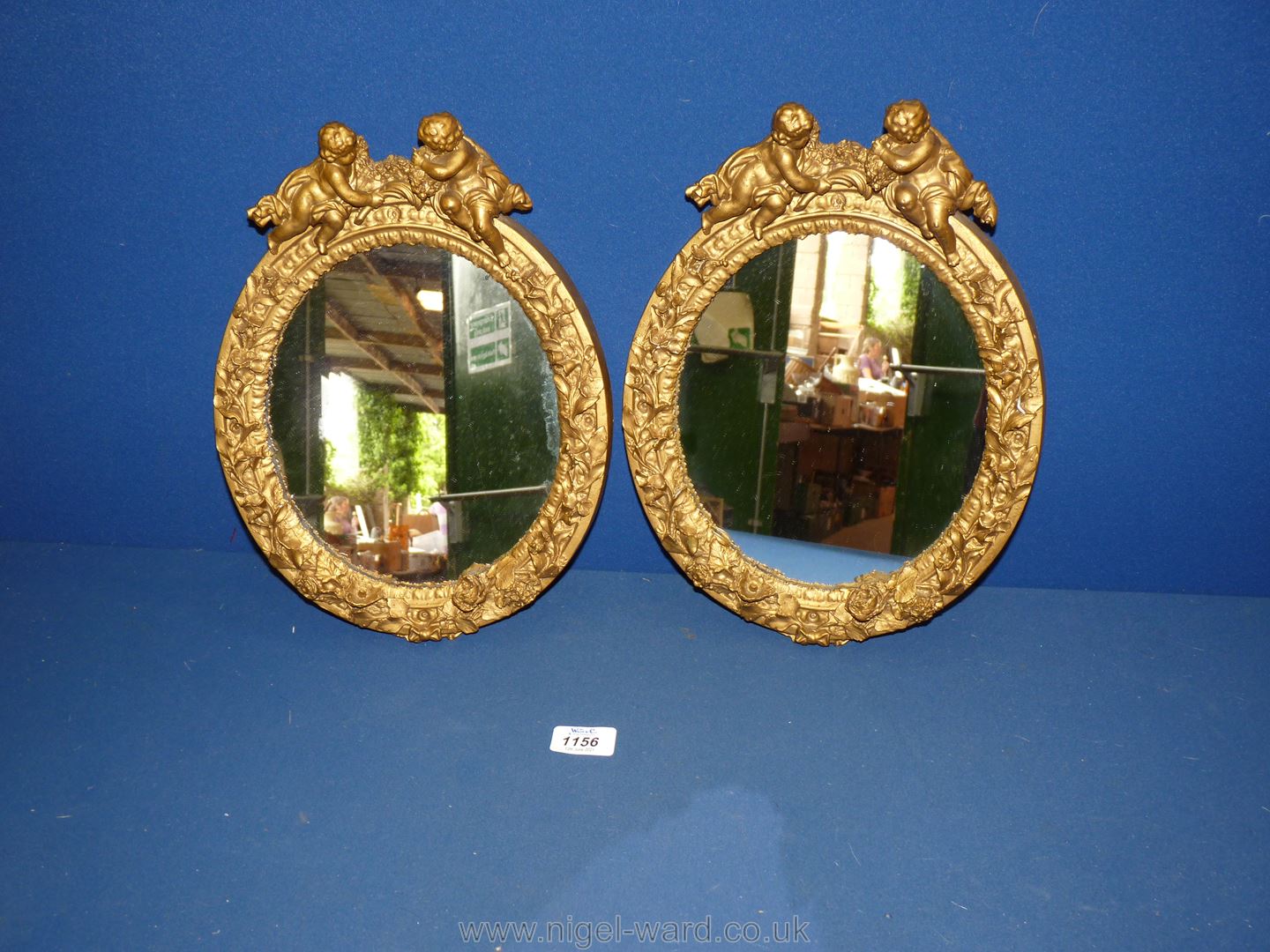 A pair of oval Mirrors in gilded frames with cherubs at the top and decorated with flowers and