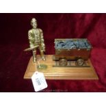 A brass figure of a coal miner and coal cart on plinth.