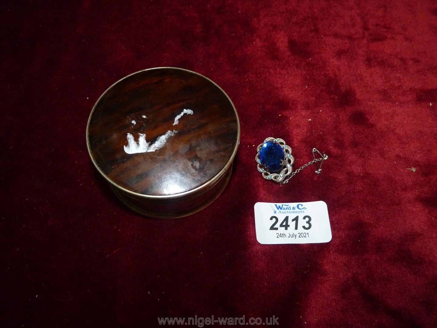 A small silver coloured trinket pot and lid with a claw set blue stoned brooch.