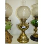 An oil lamp with a brass base and reservoir with globe shade etched with birds and leaves,