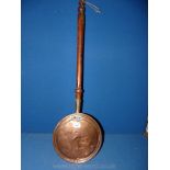 A copper warming pan with turned wood handle.