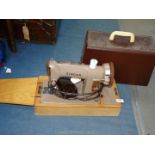 A vintage electric Singer sewing machine with contents in brown case with key.