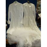 Two small wedding dresses, both long sleeved, one with lace trimming, and a net veil.