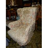 An Edwardian deep-seated wing Fireside Armchair having rounded arms and standing on turned front