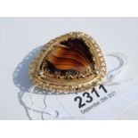 A yellow metal framed, polished, striated and faceted translucent brown stone brooch,