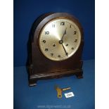 A wooden cased mantle Clock with key and pendulum, 13'' tall x 11'' wide.