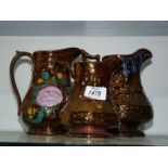 Three copper lustre jugs, the smallest by Wade, the largest with floral decoration.