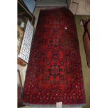 A dark red ground Rug with black and cream details, 6'6'' x 2'6''.