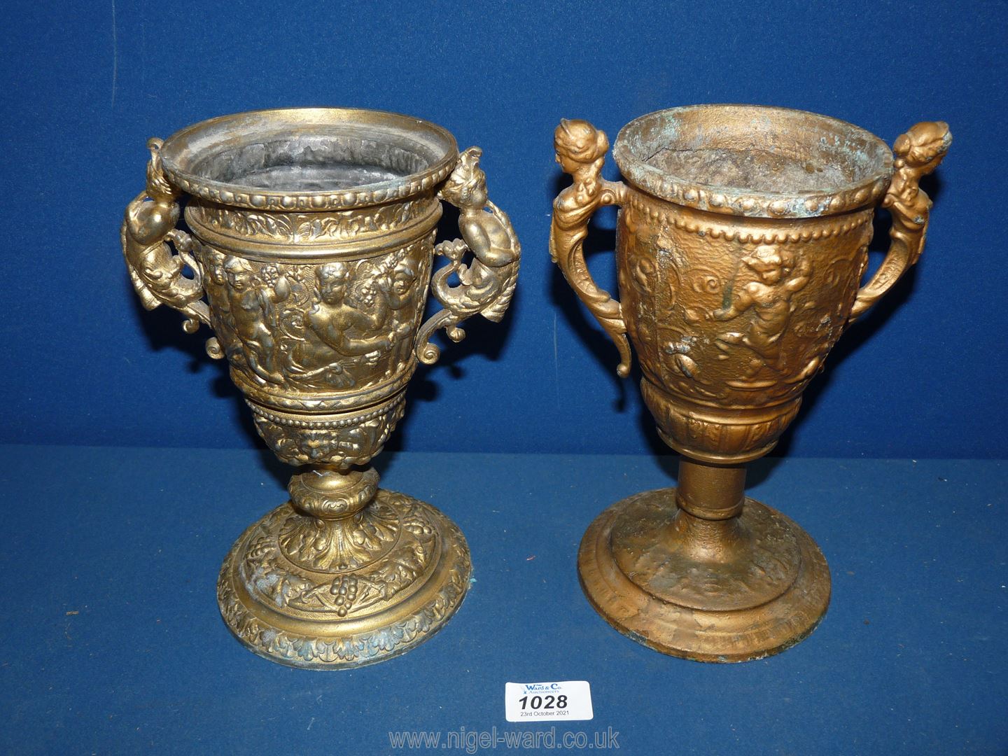 Two metal Urns in gilt colour finish, one with cherub handles, the other with lady handles,