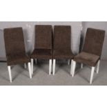 Four matching upholstered modern dining chairs raised on white painted legs.