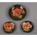 Three Moorcroft 'Hibiscus' pattern pottery, plate 18.5cm diameter, two pin dishes 11.5cm diameter (