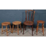 A bench wood chair with carved seat along with three stools.