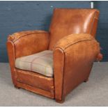 A tanned leather fireside armchair with wool tartan cushion. In tired condition.