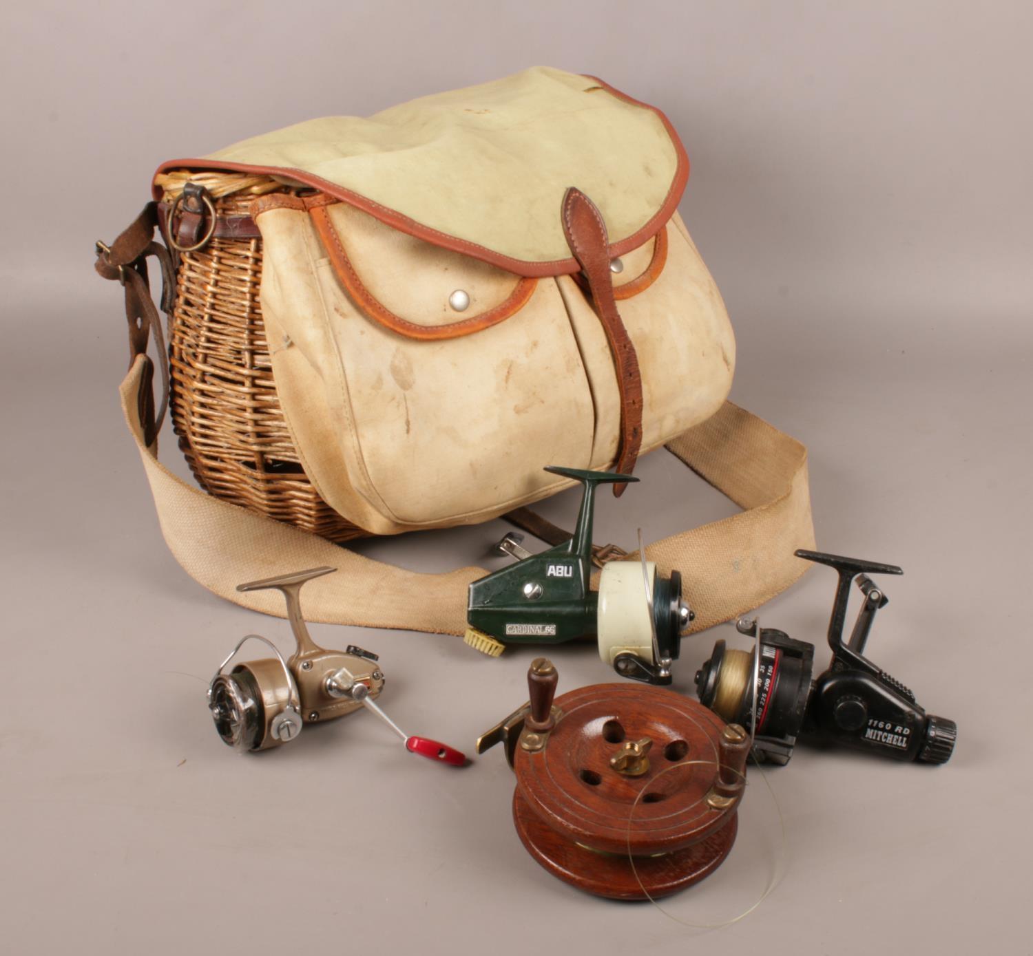 A wicker and canvas fishing creel with contents of four fishing reels. Includes Abu Cardinal 66,