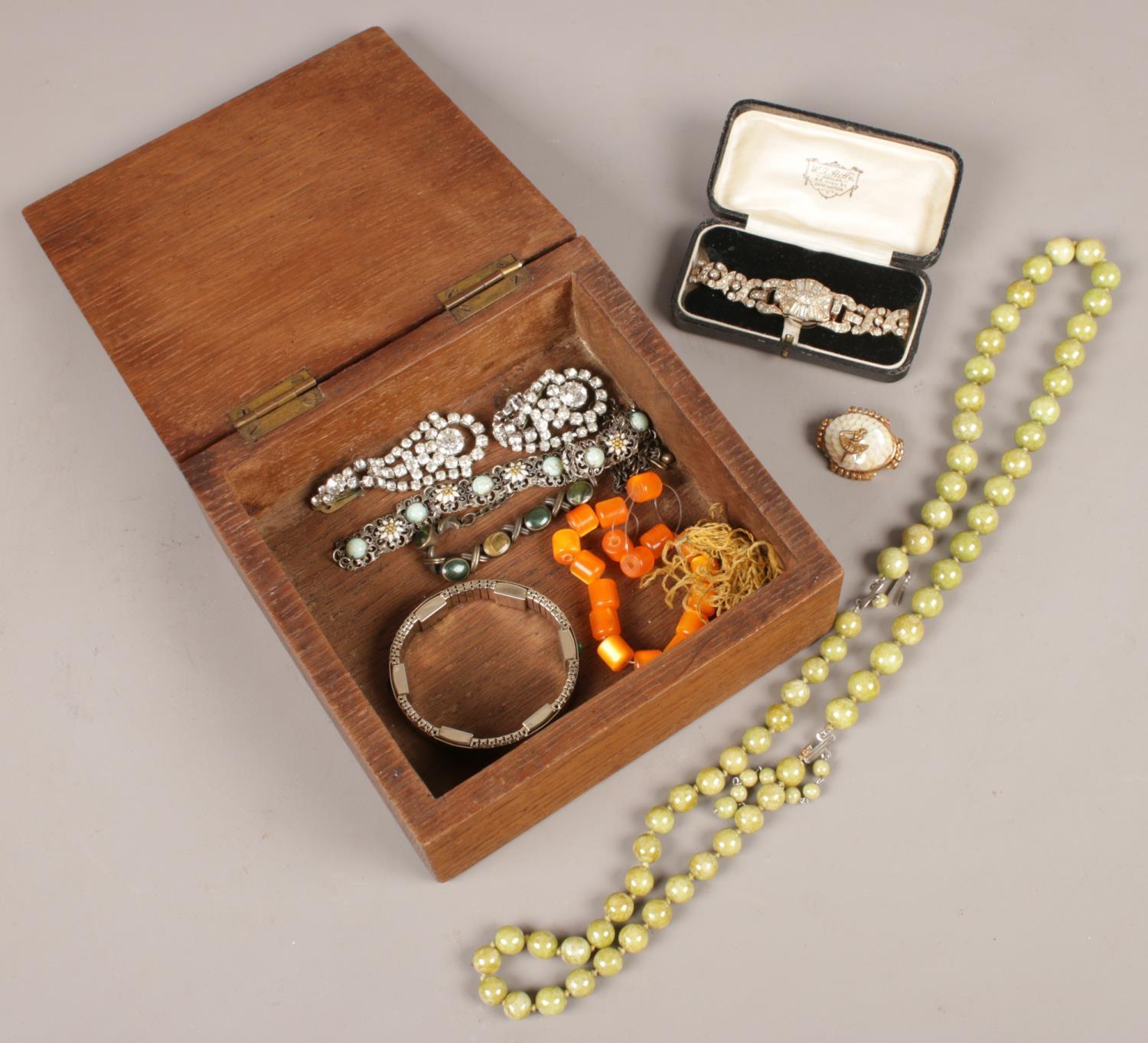 An oak box of costume jewellery. Including white paste stone set cocktail watch, earrings, vintage