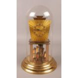 An Art Deco brass torsion clock, under glass dome. (31cm). Pendulum snapped. Chips to base of glass.