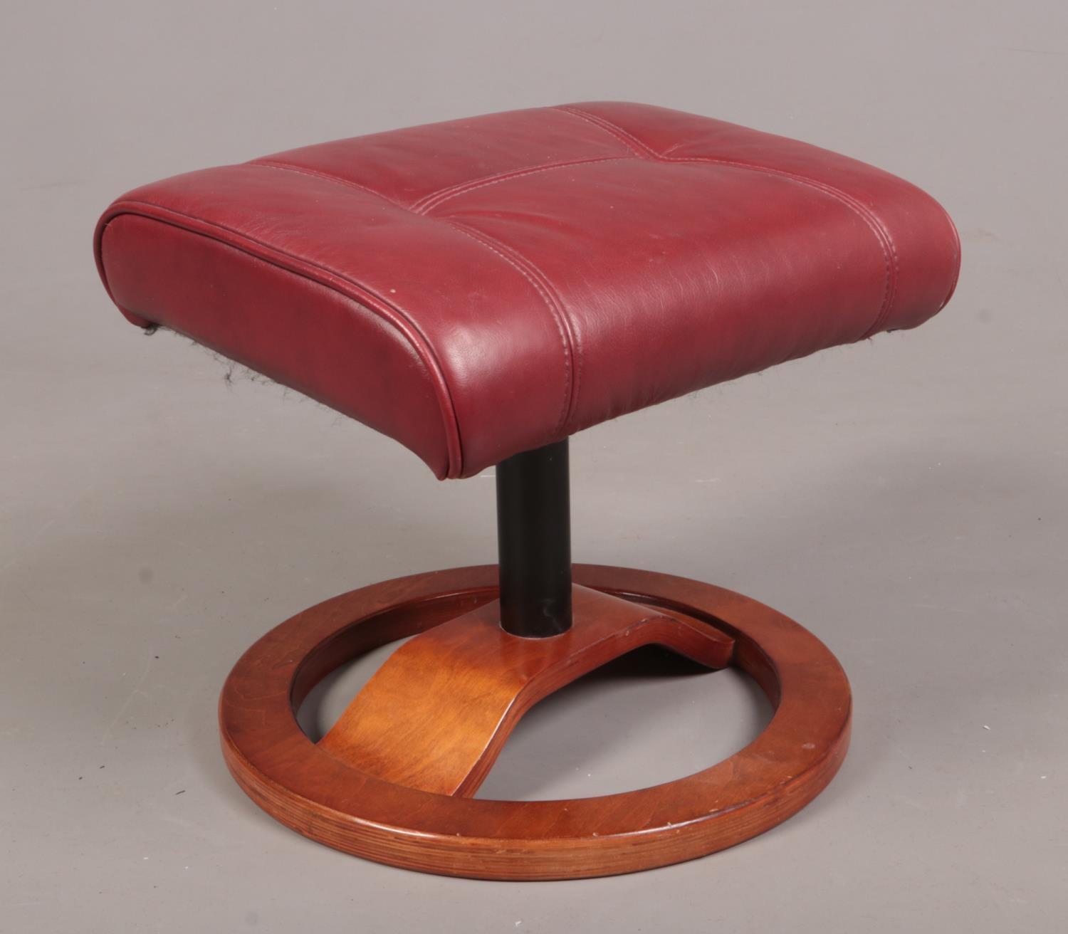 A red leather footstool with wooden base.