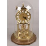 A brass Kundo torsion clock with gilt dial under glass dome.