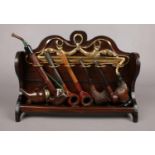 A wooden pipe rack with six wooden pipes - to include a German Bruyere pipe with metal flip top,