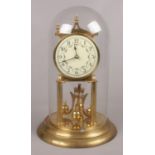 A Kieninger & Obergfell brass torsion clock with enamelled dial under glass dome.