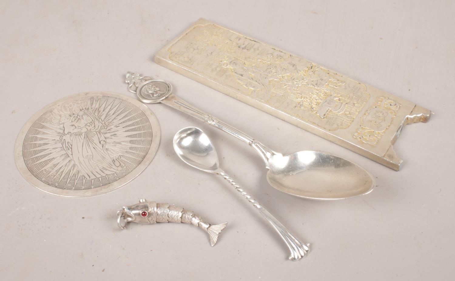 A collection of silver and white metal items. Includes fish pendant, spoons, religious disc and