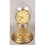 A Kaiser brass torsion clock under glass dome.