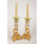 A pair of gilt metal cherub candlesticks with detachable glass gilt rimmed sconces and glass drop