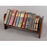 A carved oak Art Deco bookstand complete with an array of similar period hard back books, 49cm wide.