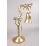 An Oriental hanging brass bell - with striker on stand modelled as a stylised dragon. H: 44cm.