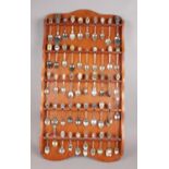An oak display rack with contents of collectors spoons. Some spoons with enamel decoration. (