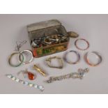 A tin of costume jewellery. Includes bangles, amber pendant on chain etc.