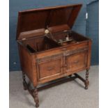 A carved and paneled oak Gilbert gramophone cabinet on barley twist supports.