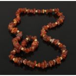 A prehistoric raw cognac amber bead and yellow metal necklace 74cm long. Good condition