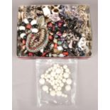 A tin of costume jewellery. Including beads, necklaces, etc